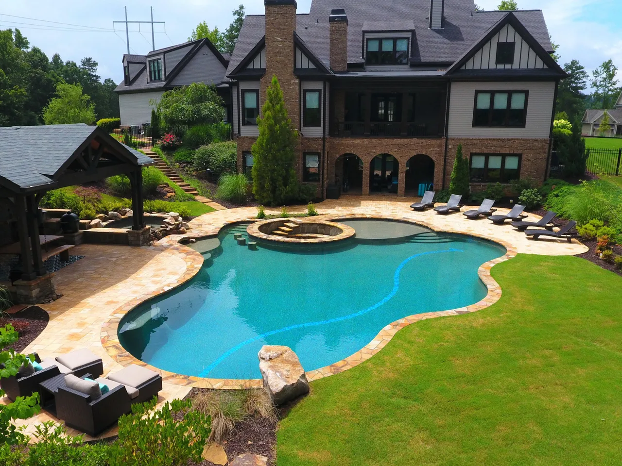 Custom freeform pool with spa and fire bowl surrounded by travertine deck and manicured lawn in Alpharetta, GA