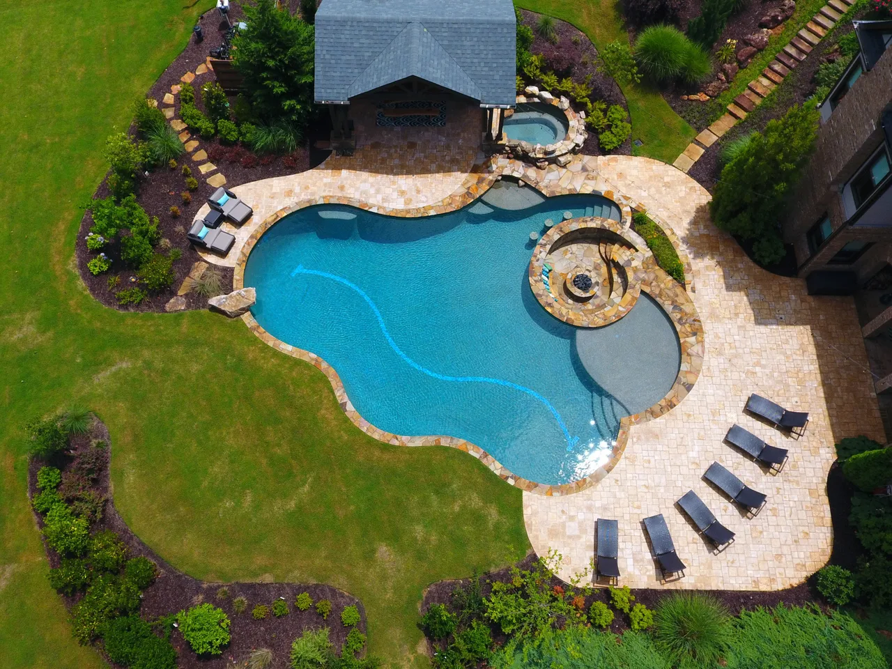 Aerial view of custom pool with spa, travertine deck, and lounge chairs surrounded by landscaping in Alpharetta, GA