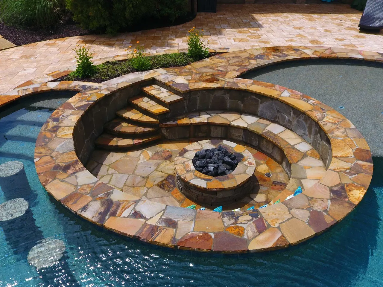 Spiral stone fire bowl on pool deck with curved seating ledges and travertine paving in Alpharetta, GA