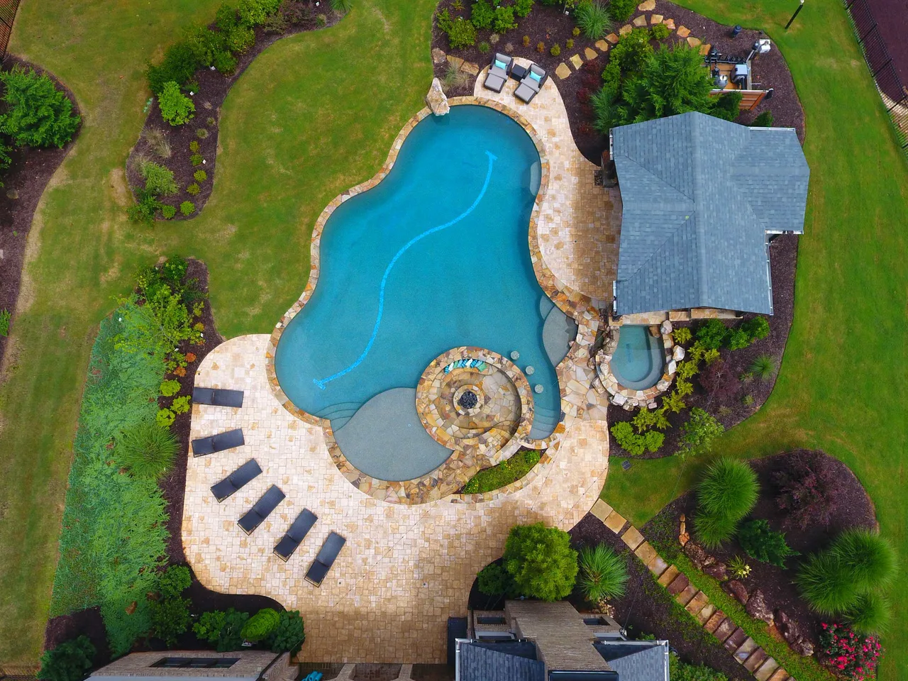 Aerial view of freeform pool with spa, travertine deck, and lounge chairs surrounded by manicured lawn in Alpharetta, GA