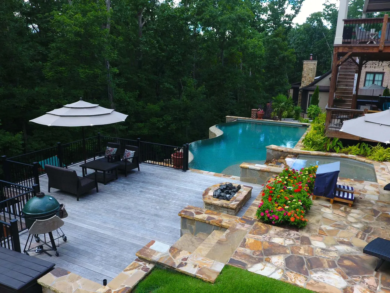 Vanishing edge pool with turquoise water, stone deck, lounge seating under umbrellas, and wooded backdrop at afternoon
