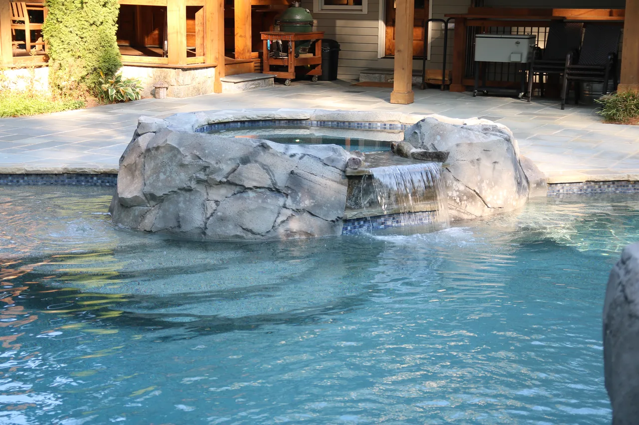 Custom pool with stone grotto waterfall feature and sunken spa surrounded by travertine deck