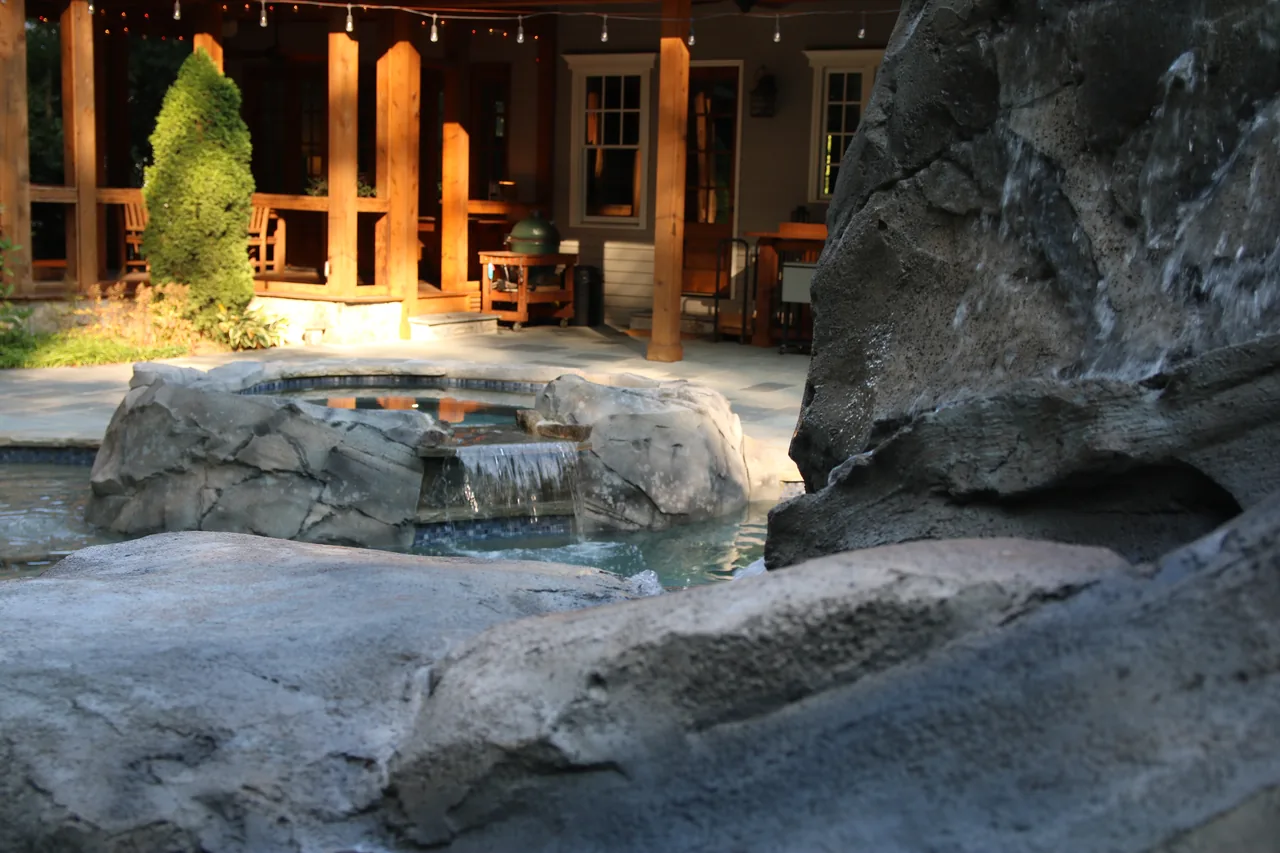 Stone grotto with waterfall feature beside illuminated pergola and pool at dusk
