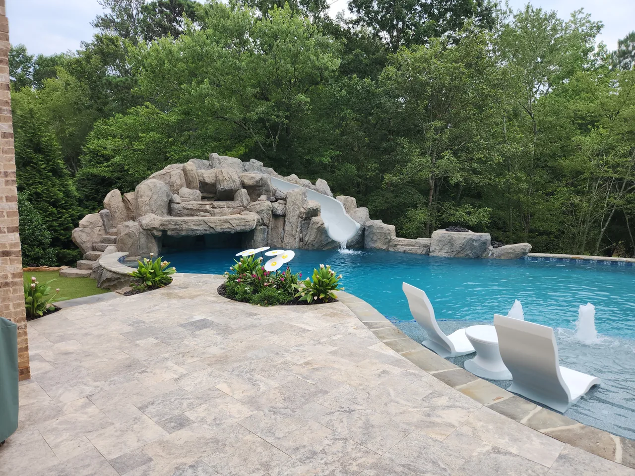 Grotto rock formation with slide, blue pool water, travertine deck, and white lounge chairs at luxury pool in Atlanta Georgia