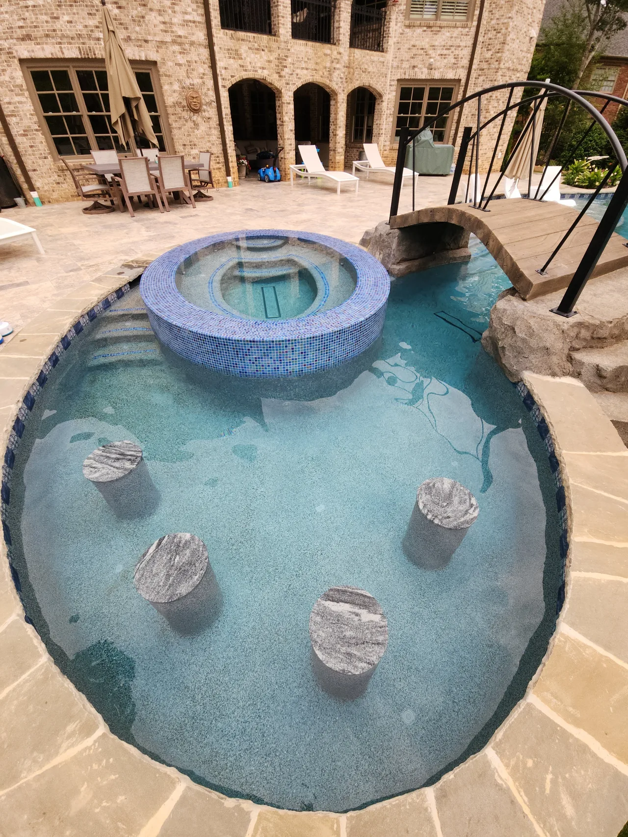 Overhead view of freeform pool with round blue tile spa, stone stepping features, and travertine deck in Atlanta Georgia