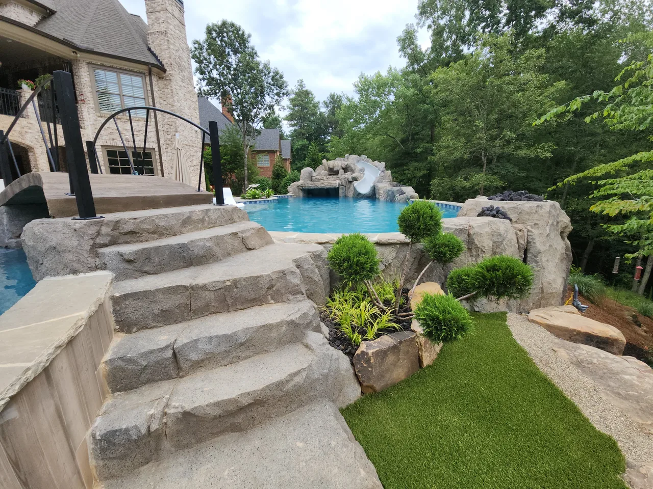 Stone steps leading down to sparkling blue pool with grotto and waterfall feature, surrounded by manicured lawn and mature trees, Atlanta Georgia