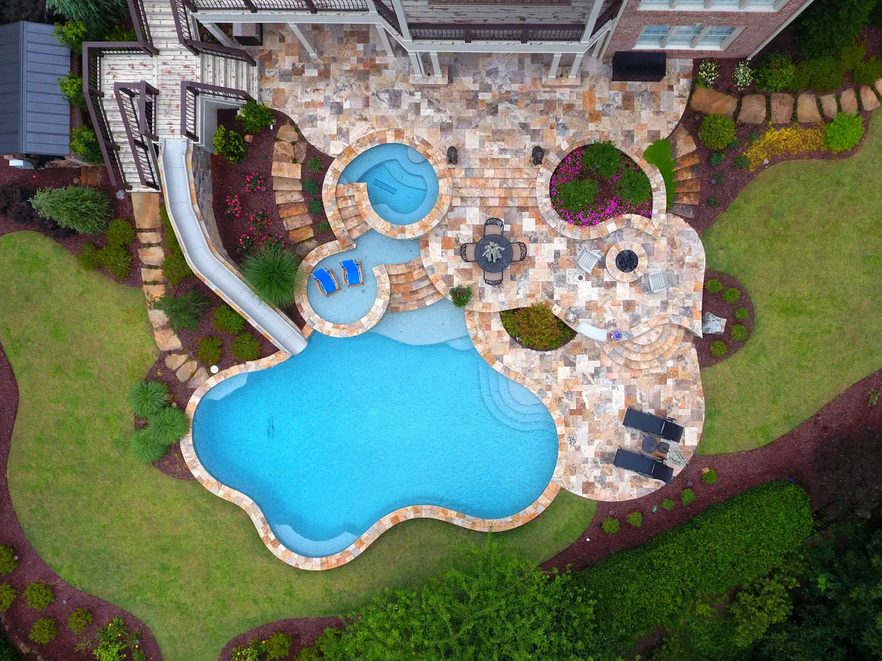 Aerial view of freeform resort pool with spa and sun shelf surrounded by brick patio and landscaping in Johns Creek, GA
