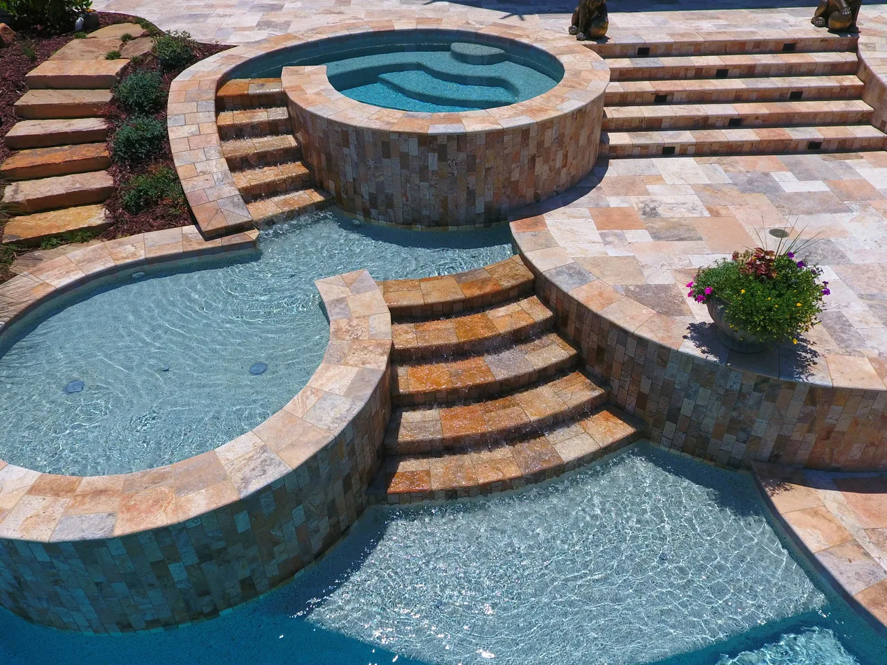 Overhead view of three-tier freeform pool with round spa, travertine decking, and stacked stone steps in Johns Creek, GA