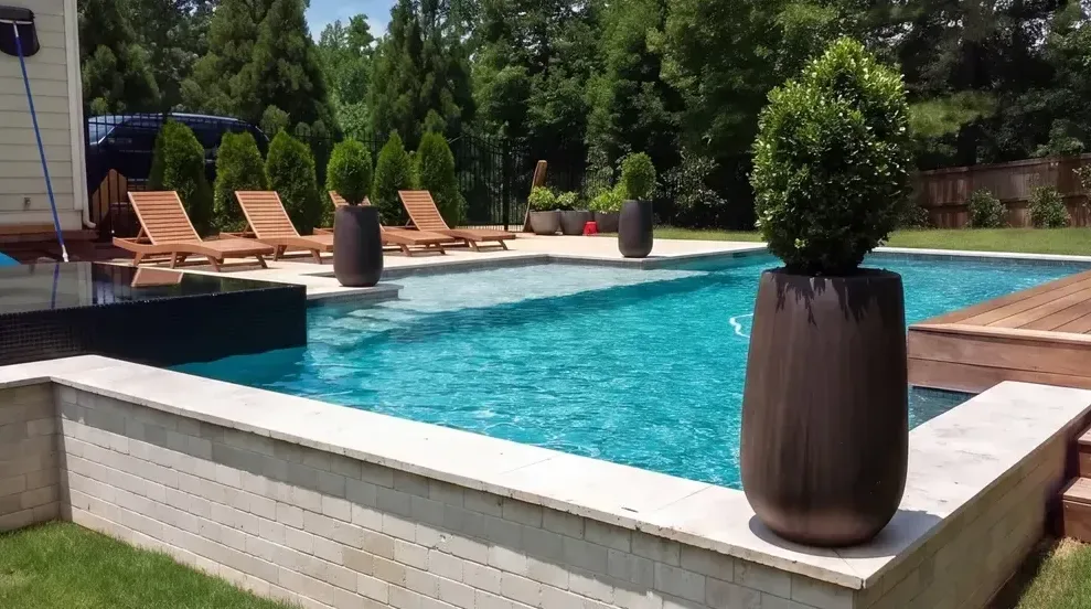 Modern custom pool with clean white deck edge, bright blue water, and lounge chairs on composite decking surrounded by trees in Lake Lanier, GA