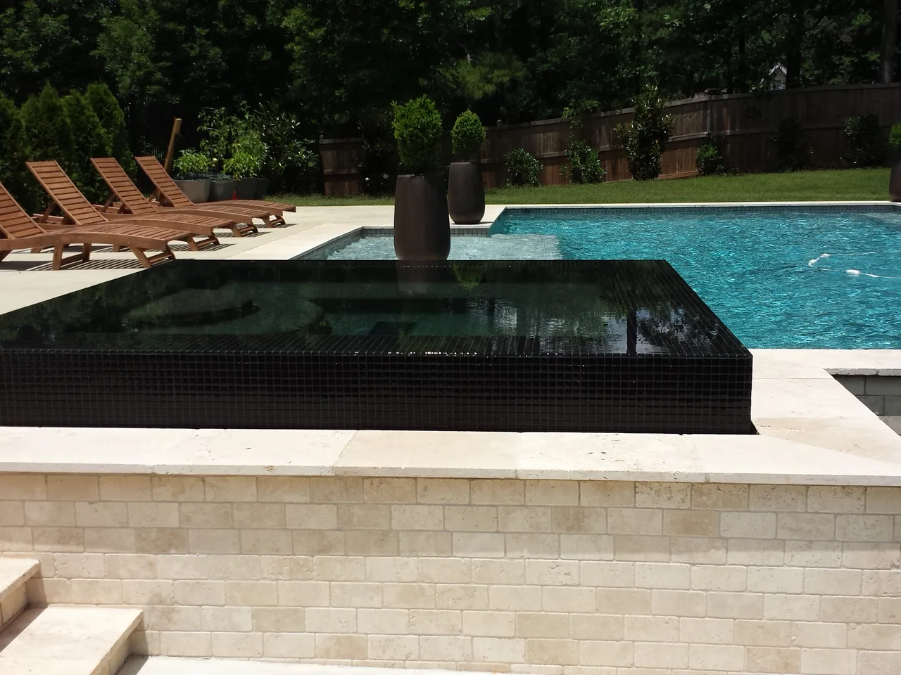 Modern spa with black tile and stone surround beside turquoise pool and lounge chairs near Lake Lanier, GA