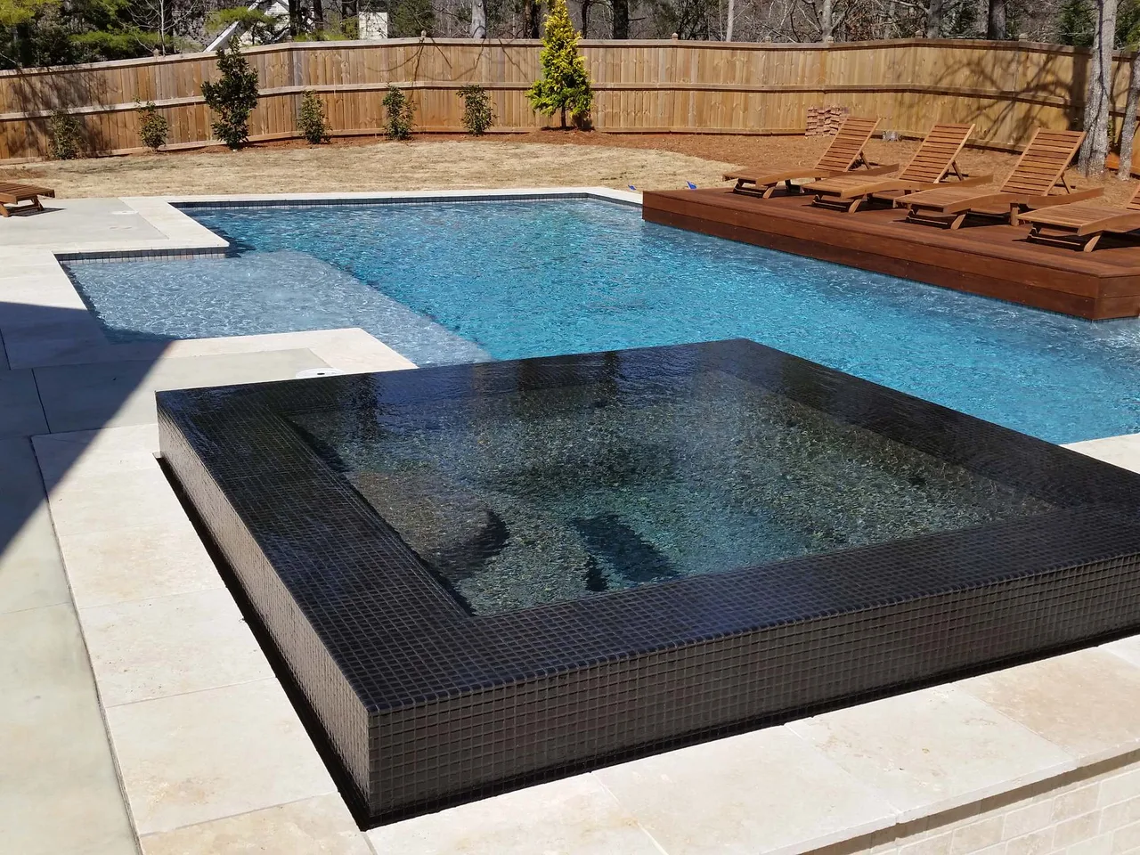 Black tile spa with water feature in foreground, large swimming pool and wooden lounge deck in background, Lake Lanier, GA