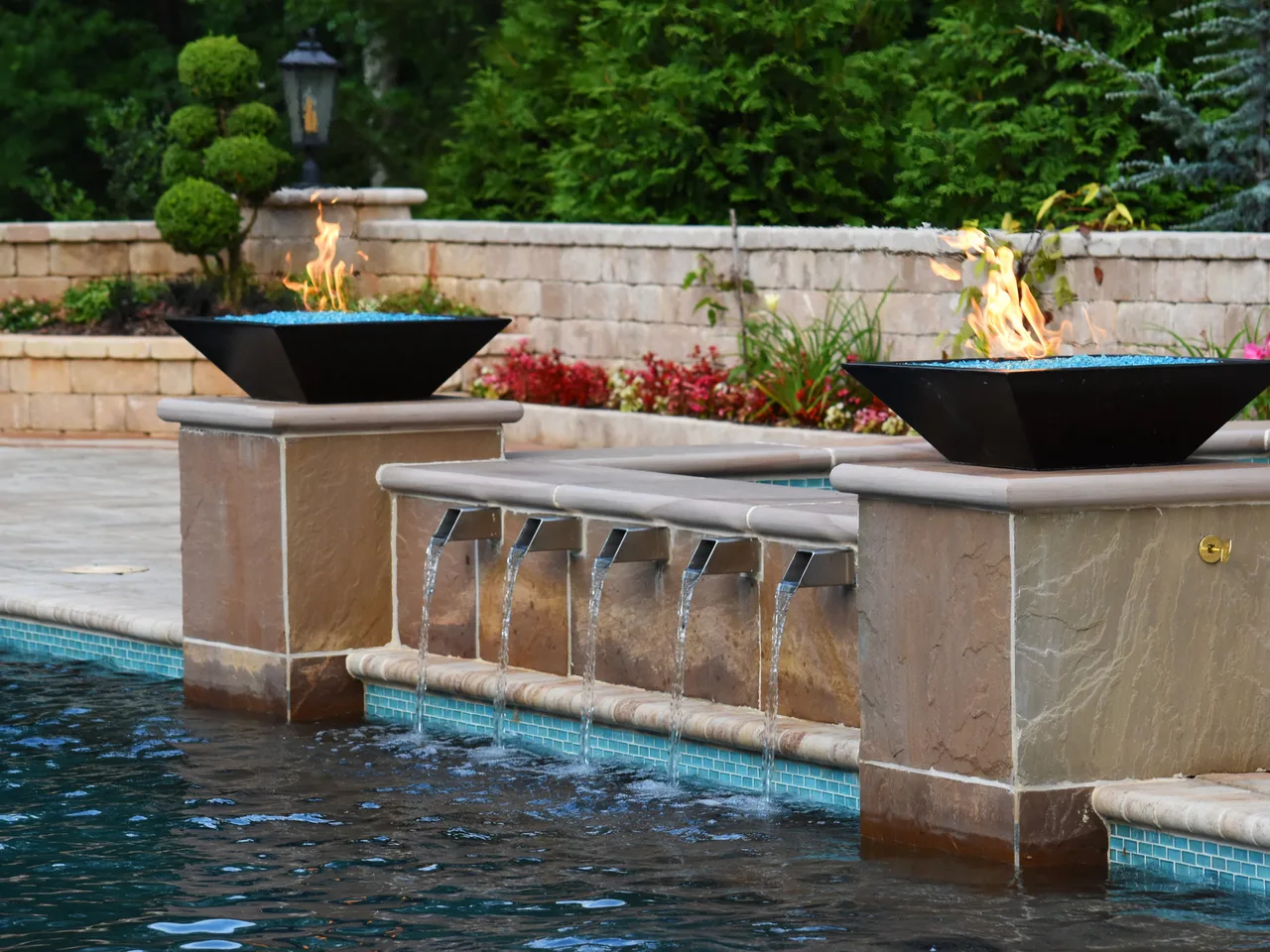 Travertine water feature wall with sheer descents and fire bowls along pool edge in Marietta, GA
