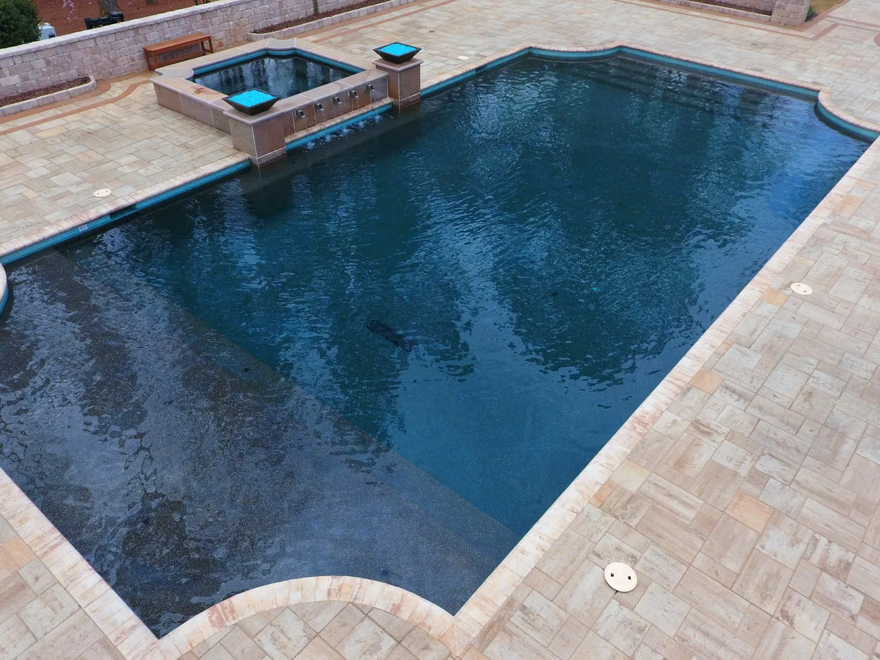 Contemporary rectangular swimming pool with curved corners and dark blue interior, spa adjacent, travertine deck in Marietta, GA