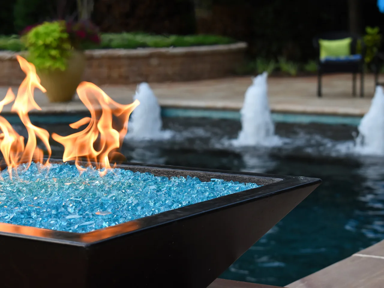 Fire bowl with blue glass beads and flames overlooking pool with fountain water features at dusk in Marietta, GA