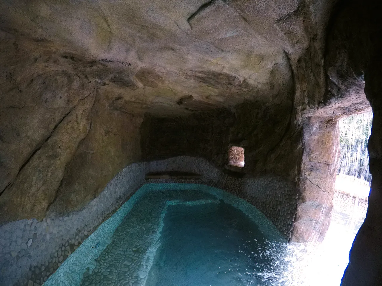 Underground grotto with turquoise water, stone walls and ceiling, natural light from opening on right
