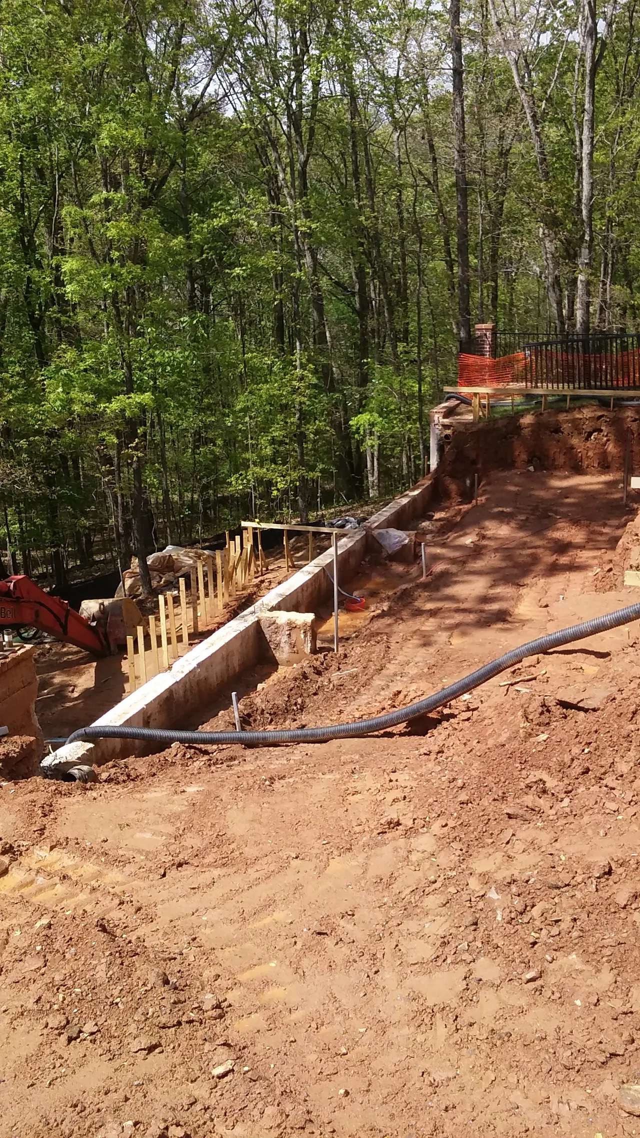Custom pool construction site with wooden forms, red brick chimney, metal railing, and dense forest backdrop in Marietta, Georgia