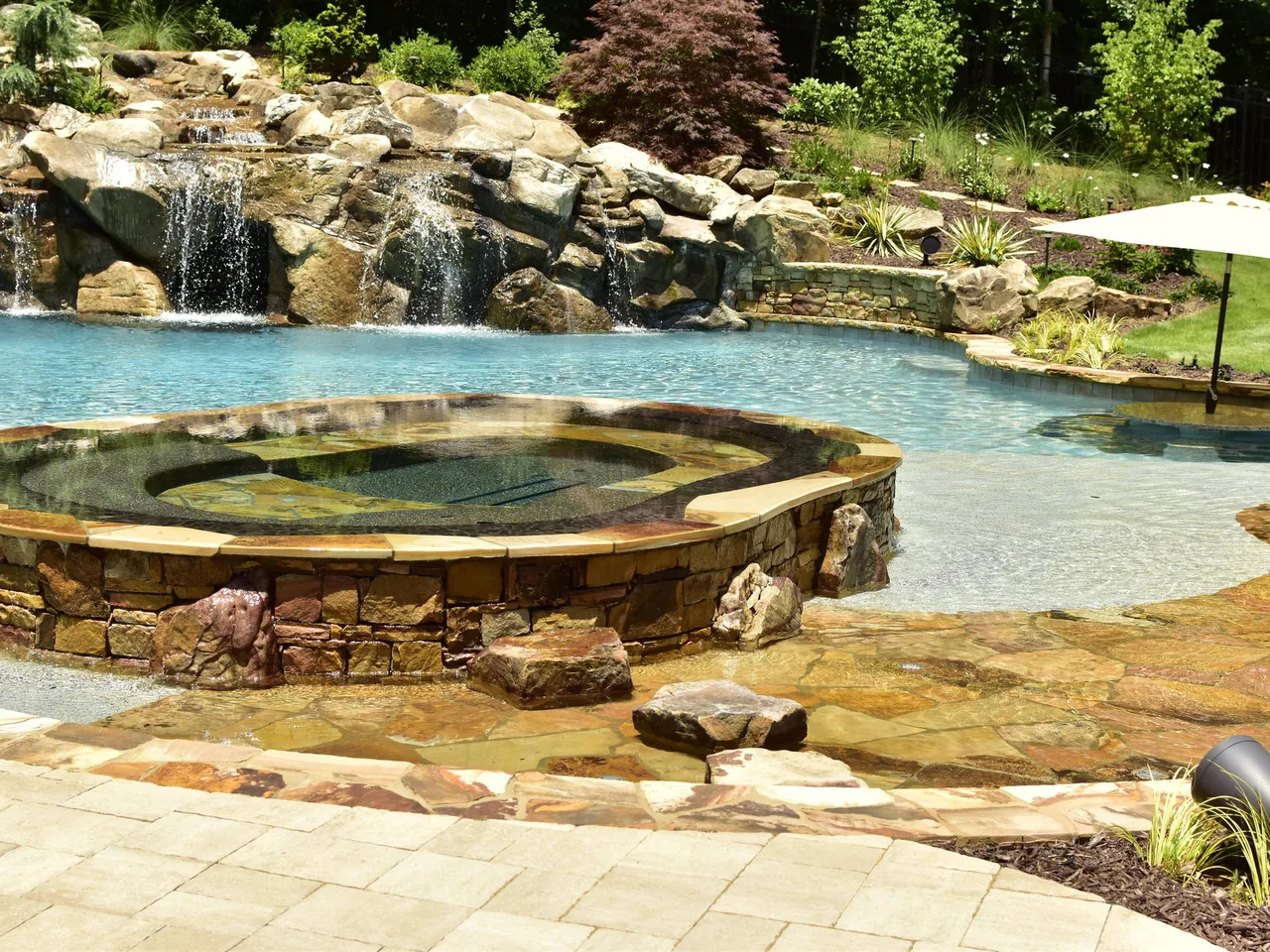 Stacked stone spa with natural surround adjacent to freeform pool and waterfall feature