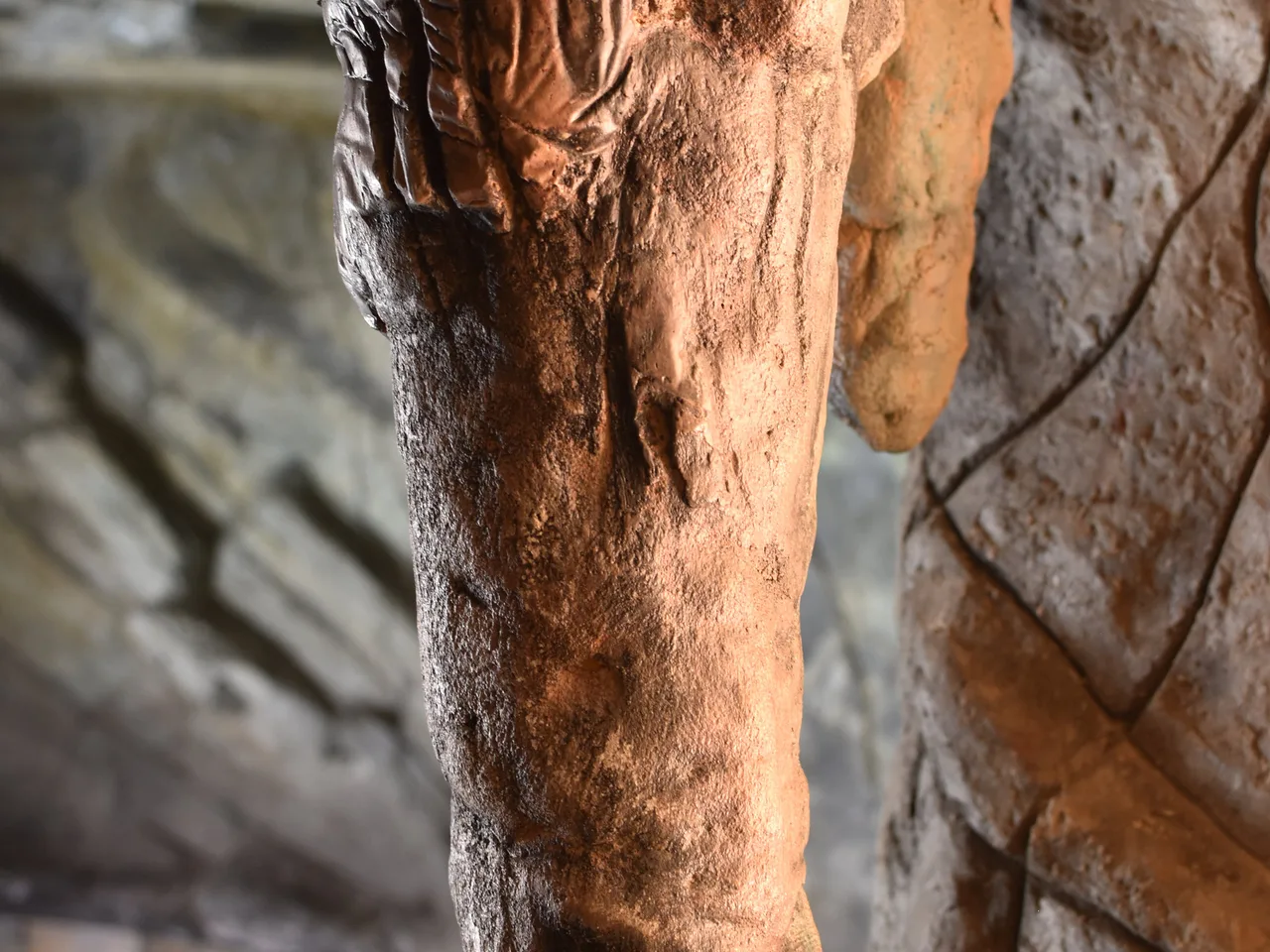 Textured travertine column with water cascading down, pool water visible in soft focus background
