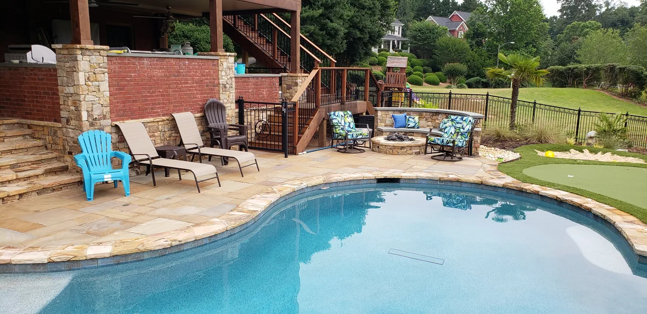 Curved pool with travertine deck, stone-clad raised wall, sheer descent, and integrated fire pit surrounded by lounge chairs