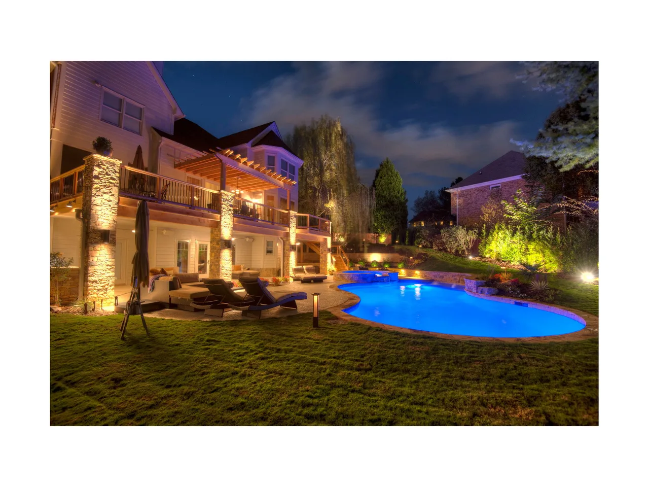 Illuminated custom pool with blue LED lighting, spa, lounge chairs, and multi-level deck at dusk in Roswell, GA