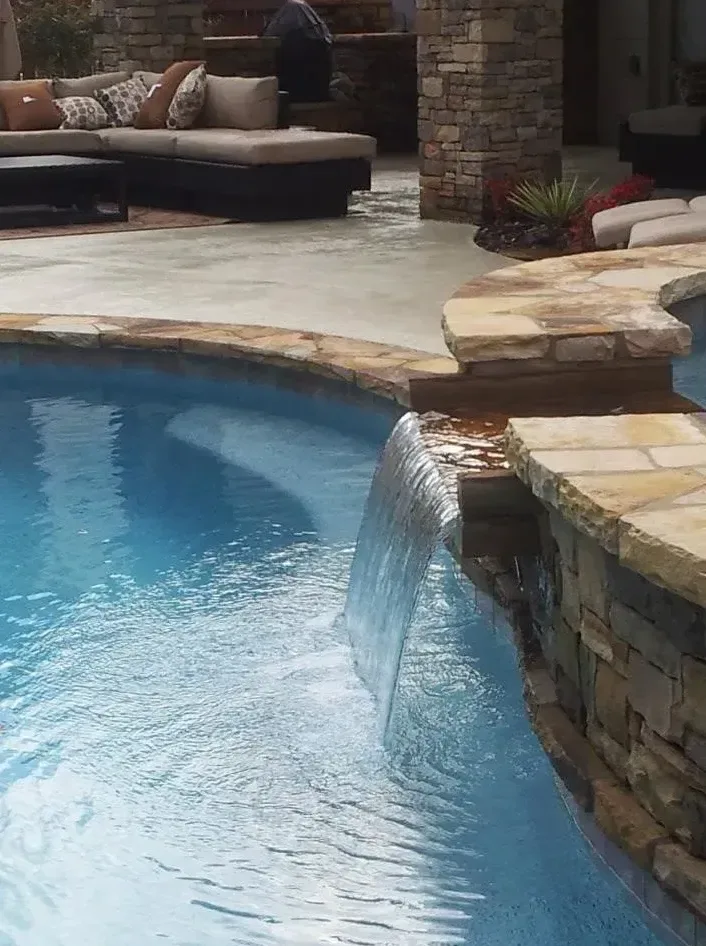 Water cascading from stone sheer descent into blue pool with travertine deck and lounge area in background, Roswell, GA