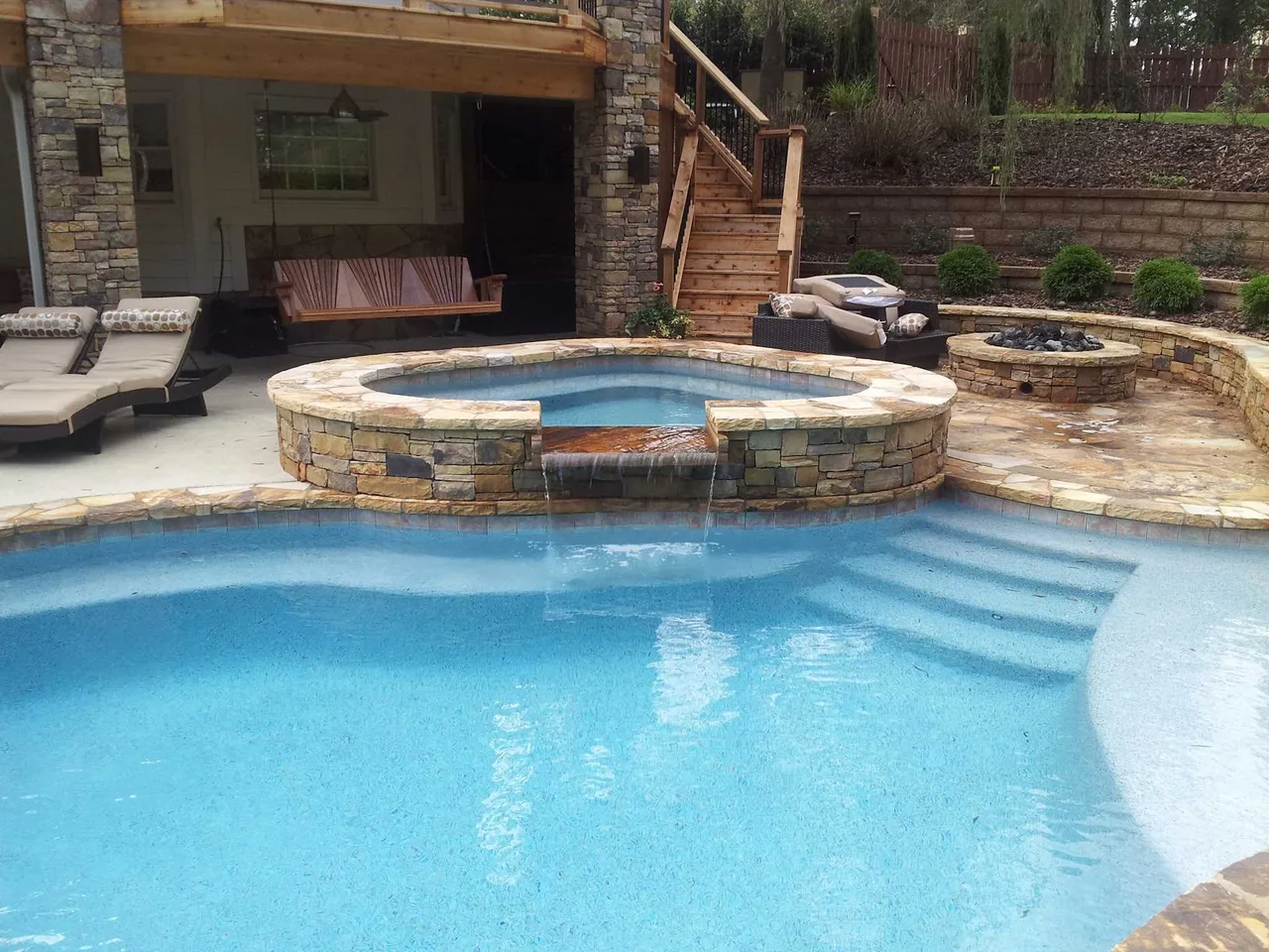 Curved stone spa with waterfall feature overlooking expansive swimming pool in Roswell, GA