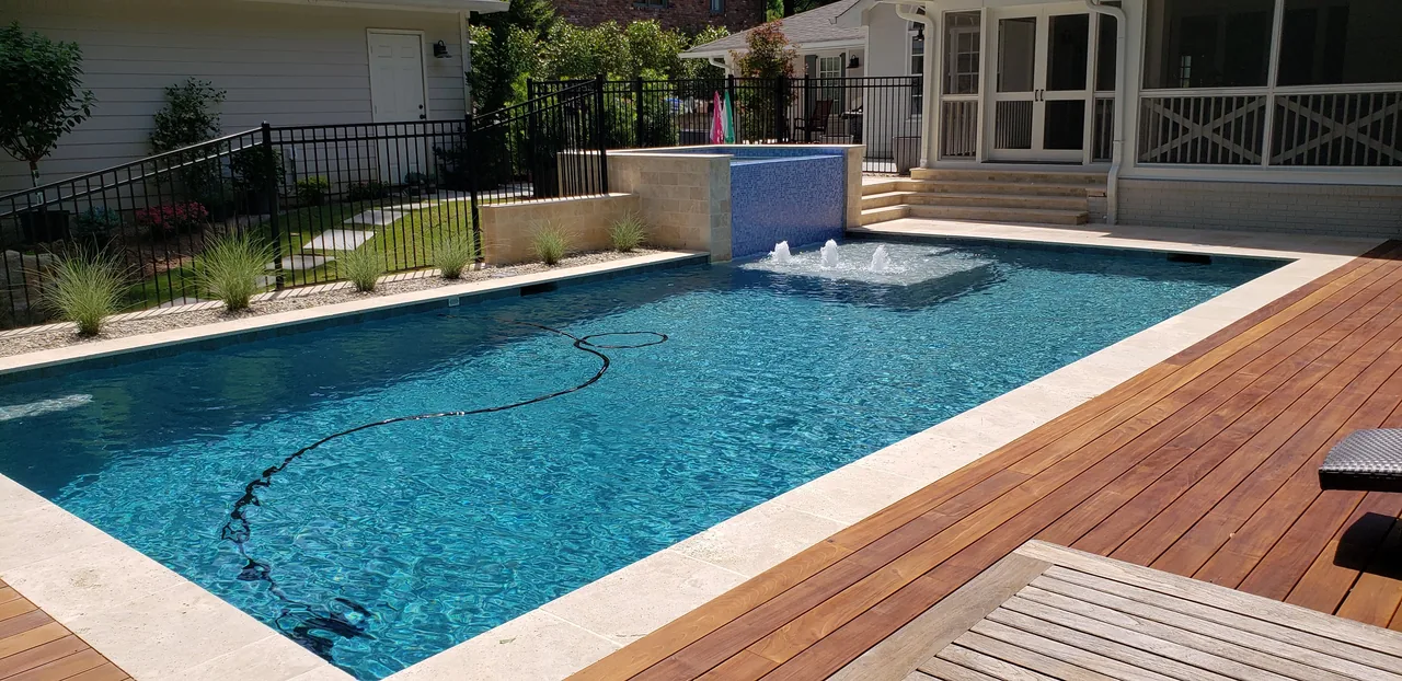 Modern linear swimming pool with travertine coping, ipe wood deck, and overflow spa with water feature in Atlanta Georgia