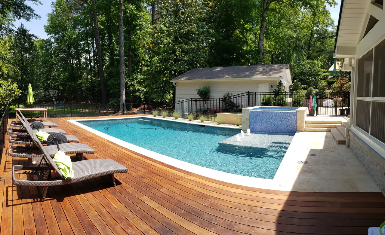 Modern linear pool with overflow spa, ipe wood deck, travertine coping, lounge chairs, and tree-lined backyard in Atlanta, Georgia