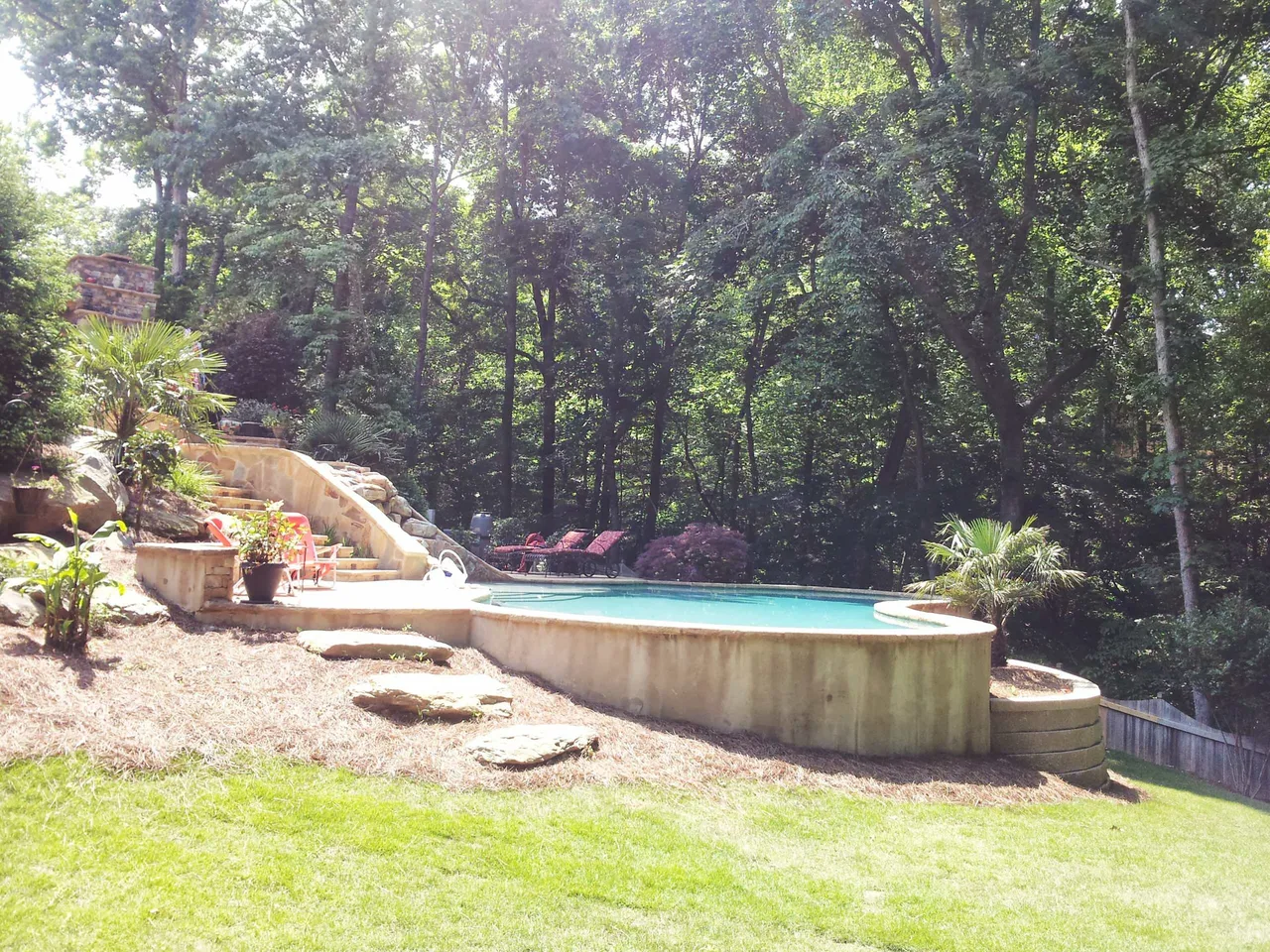 Curved custom pool with sun shelf and integrated spa surrounded by mature trees and landscaping in Suwanee, GA
