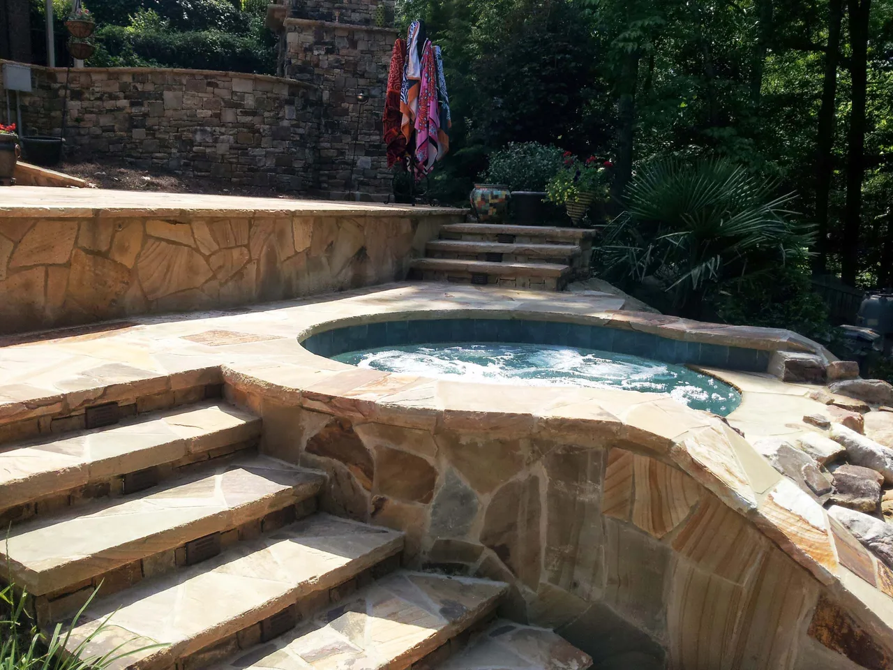 Curved pool with stone deck and integrated spa, surrounded by tiered travertine steps and stone retaining walls in Suwanee, GA