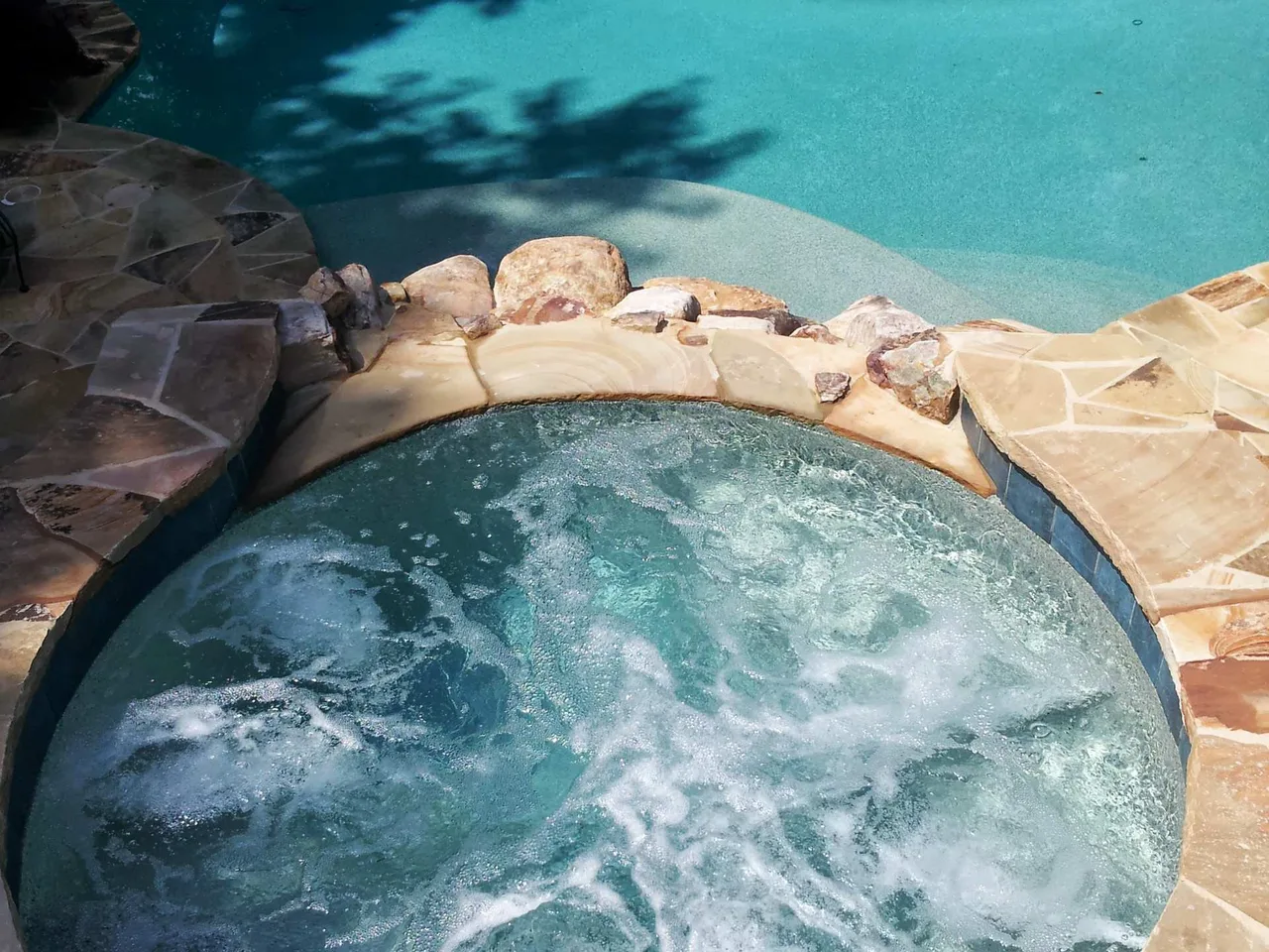 Circular spa with bubbling jets and travertine deck border adjacent to pool in Suwanee, GA