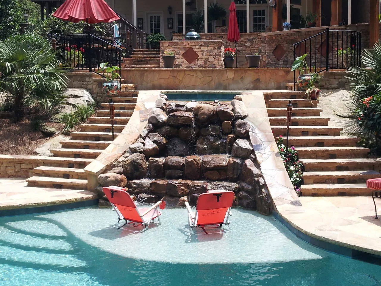 Rock waterfall feature with sheer descent into resort-style pool, flanked by tiered brick steps and lounge chairs in Suwanee, GA