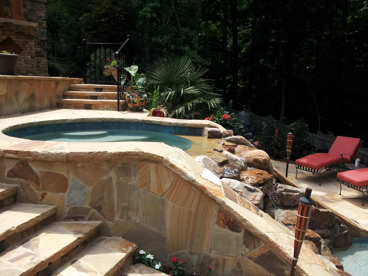 Curved vanishing edge pool with spa, natural stone decking, and stacked rock spa surround in Suwanee, GA