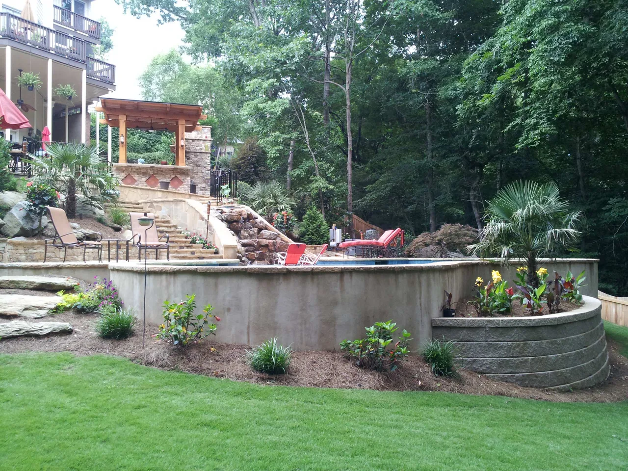Concrete pool shell with stone spa and wooden pergola structure set into hillside landscape with mature trees in Suwanee, GA