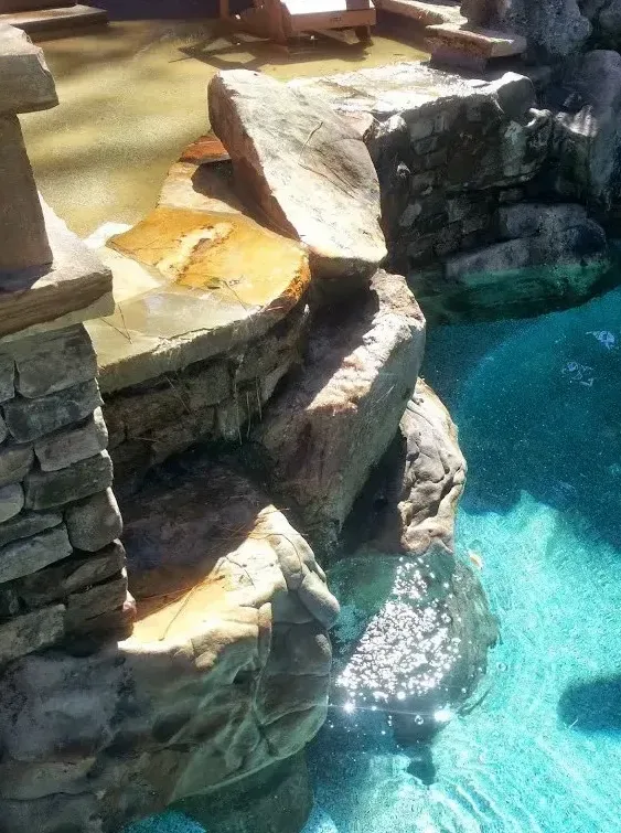 Aerial view of free-form pool with turquoise water, natural stone outcroppings, and sun shelf seating areas