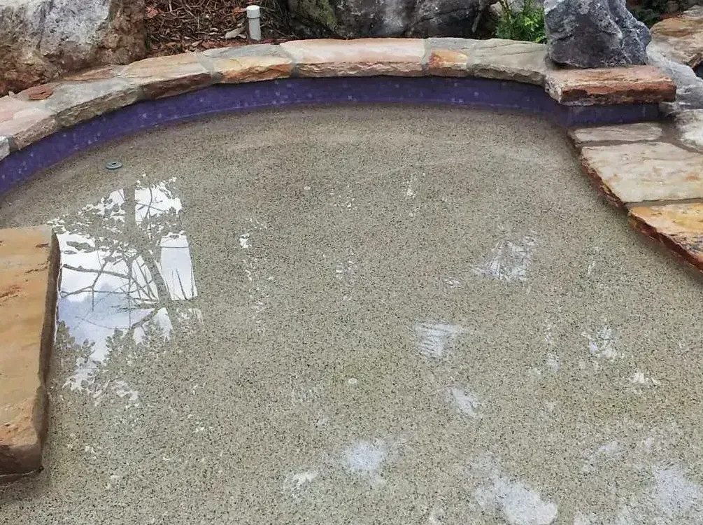 Curved free-form pool with natural stone coping and sun shelf visible during construction phase
