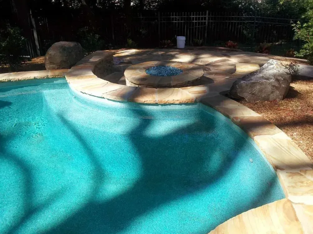 Turquoise free-form pool with sun shelf and natural boulder water feature on travertine deck during daytime