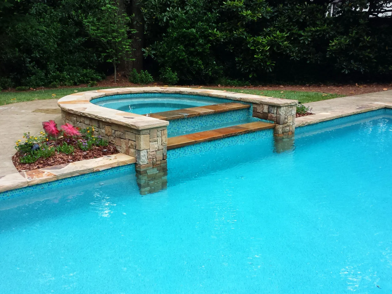 Custom lap pool with stone and wood bridge connecting to elevated spa, travertine deck, pink flowering shrubs, afternoon light, Atlanta GA
