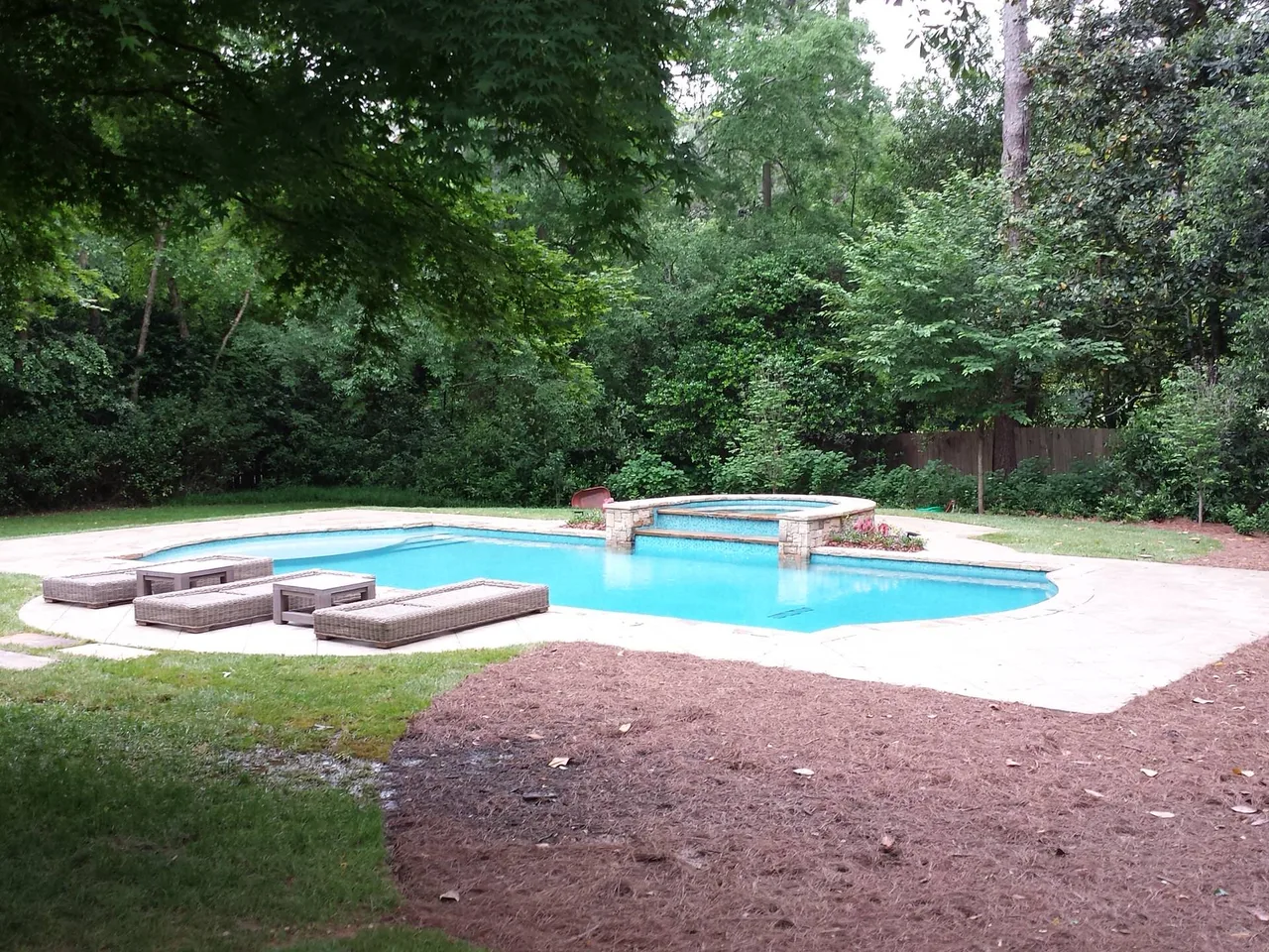 Curved luxury pool with sun shelf lounge area and brick water feature surrounded by mature trees in Atlanta, Georgia
